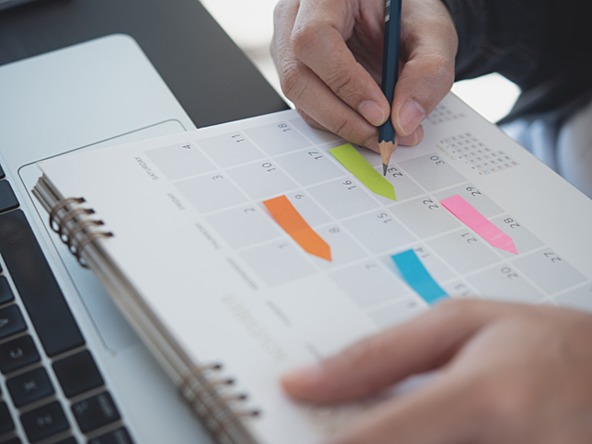 person planning dates in a calendar with a pencil and coloured sticky notes